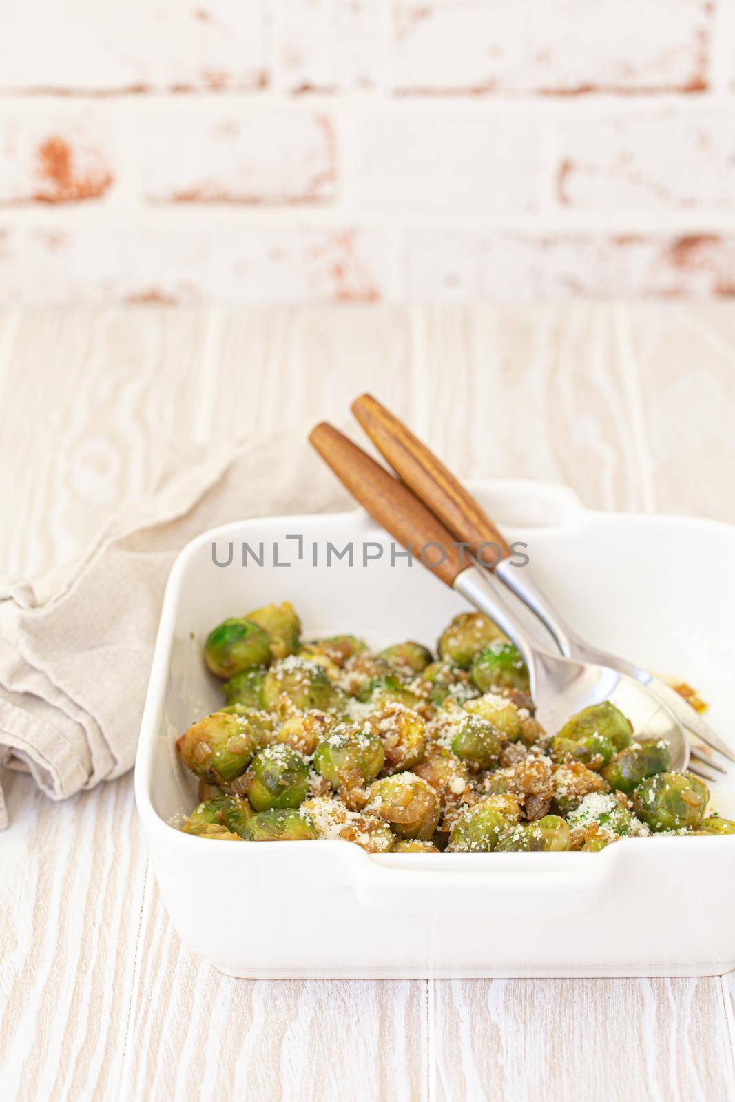 Healthy vegetarian dish roasted brussels sprouts with butter and parmesan cheese in white ceramic casserole close up on wooden table angle view, vegan food