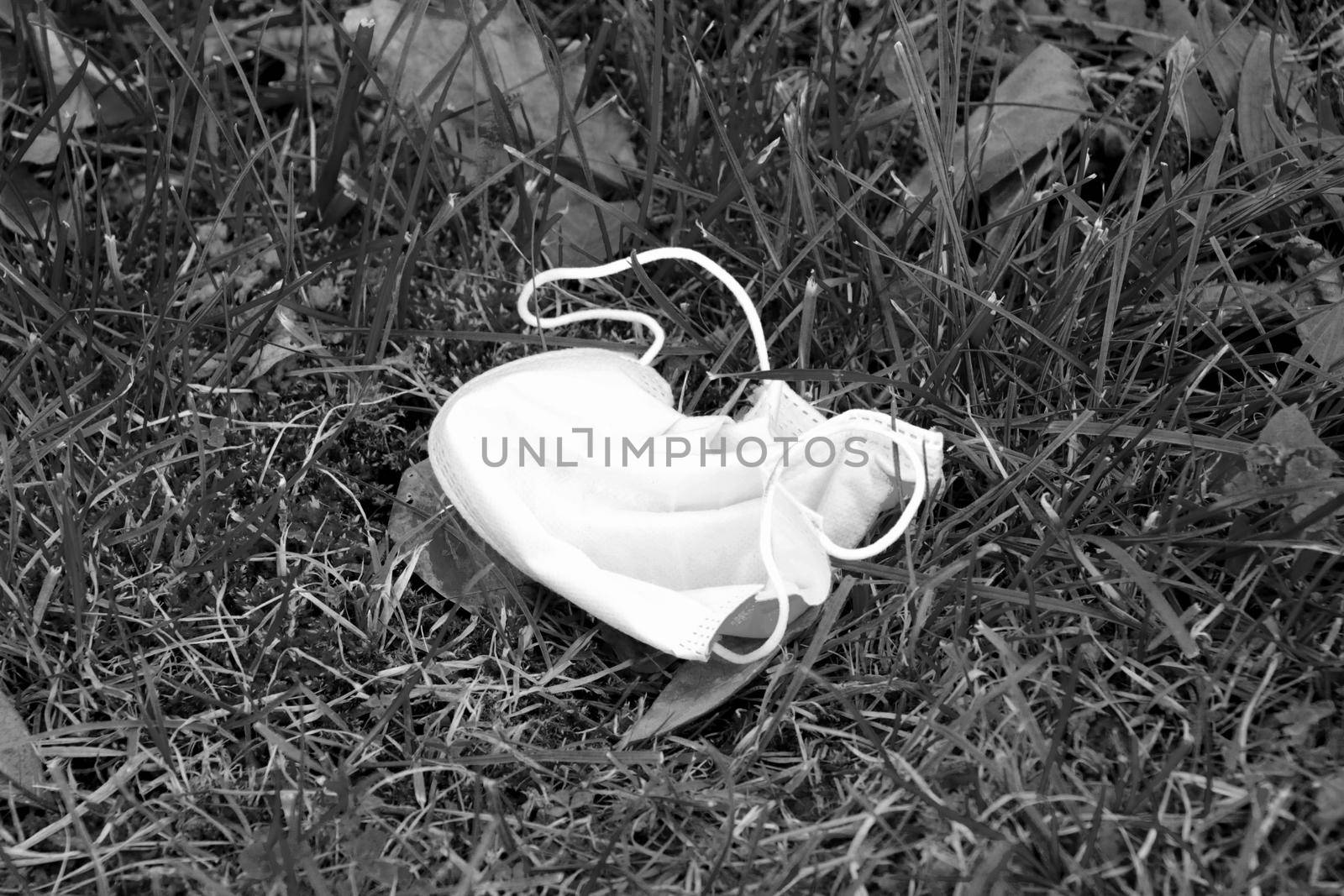 Black and white photo. Used medical mask on the ground