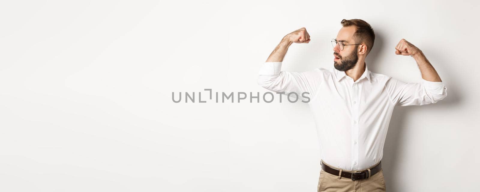 Successful businessman flex biceps, showing muscles and looking confident, feeling strong, standing over white background.