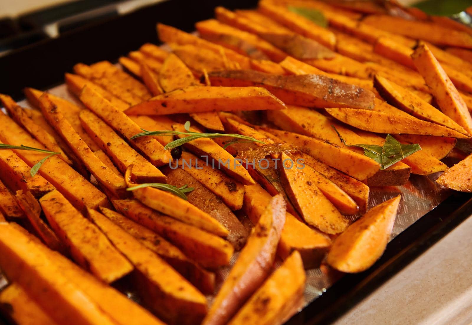 Sliced wedges of organic sweet potato, drizzled with olive oil and seasoned with fragrant culinary herbs on baking sheet by artgf