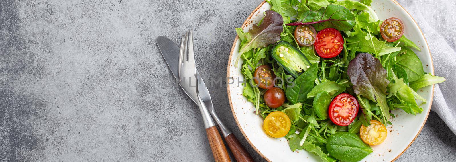 Vegetables healthy salad with red and yellow cherry tomatoes, pepper and green salad leafs on white rustic ceramic plate on gray concrete background top view, healthy food and diet concept, copy space