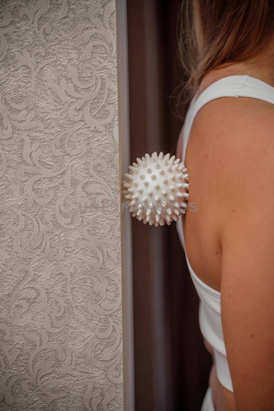 Athletic slim caucasian woman doing thigh self-massage with a massage ball indoors. Self-isolating massage.