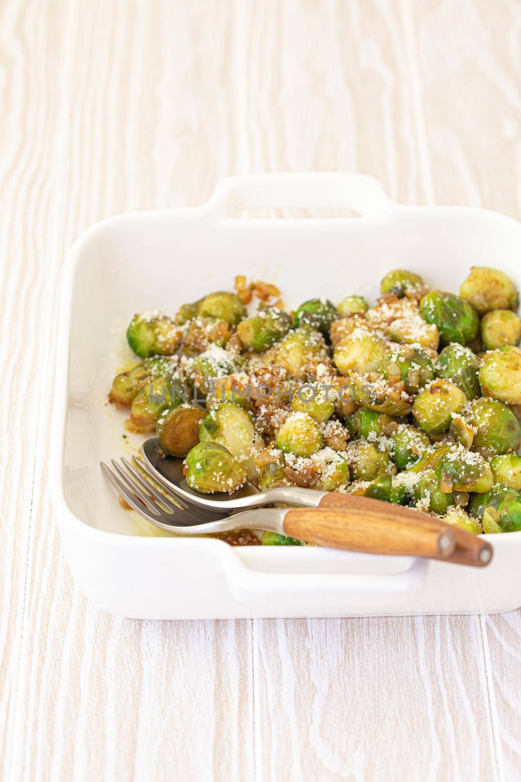 Healthy vegetarian dish roasted brussels sprouts with butter and parmesan cheese in white ceramic casserole close up on wooden table angle view, vegan food