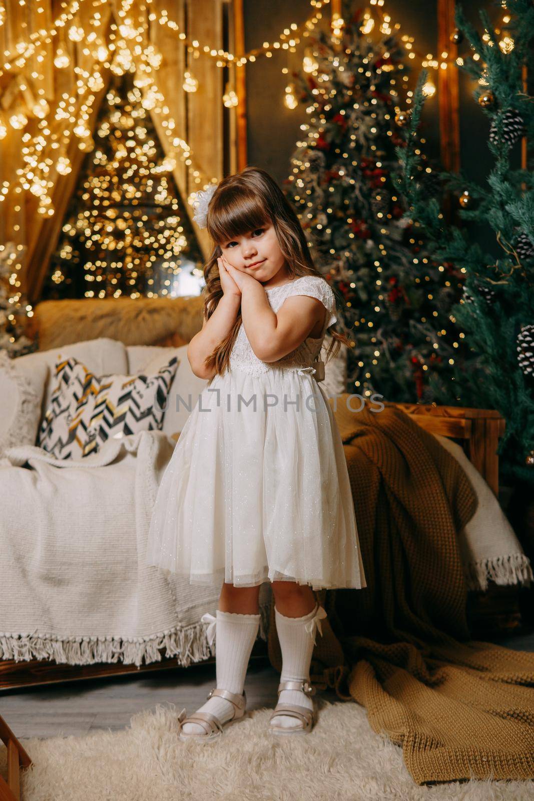 A girl in a festive light dress next to a Christmas tree, lights of garlands in the background. The concept of New Year holidays.