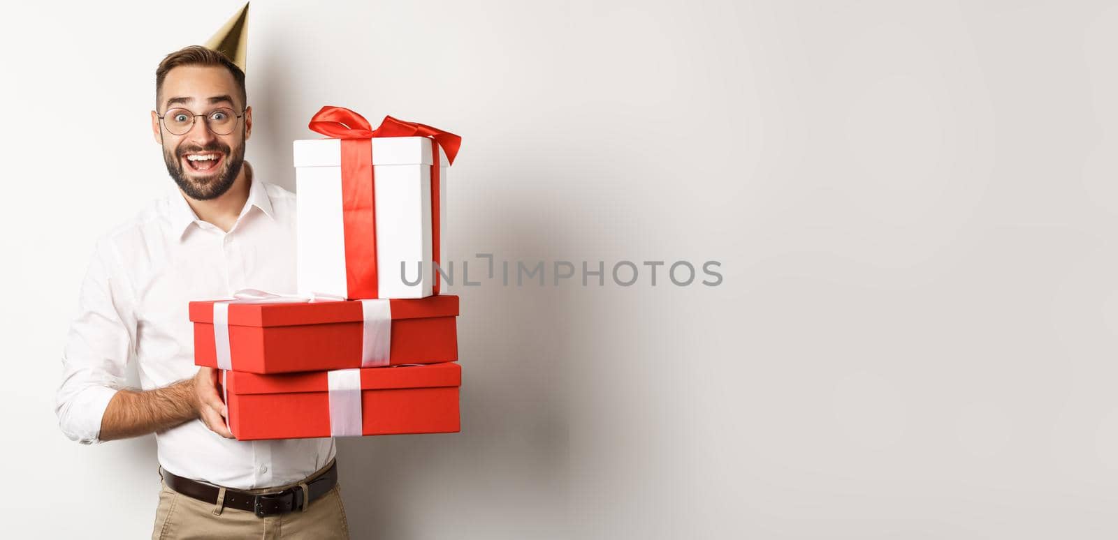 Holidays and celebration. Happy man receiving gifts on birthday, holding presents and looking excited, standing over white background.