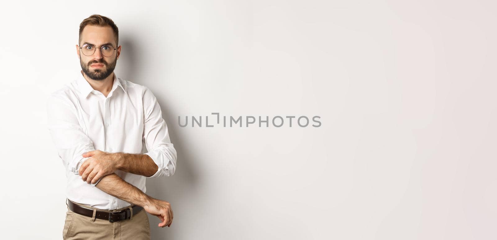 Angry man roll up sleeves and looking offended, getting ready to fight, standing over white background.