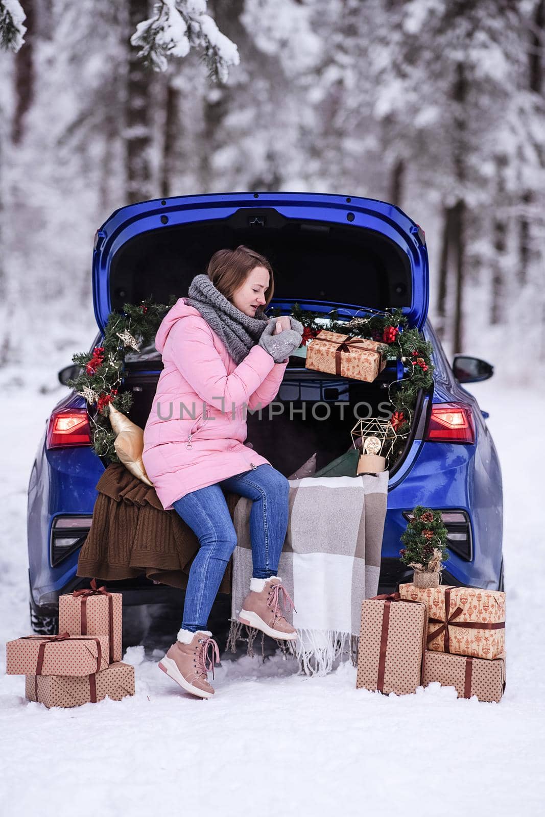 A woman in winter clothes drinks a hot drink sitting in a car decorated in a New Year's way. Traveling by car through the forest. A trip before Christmas by Annu1tochka