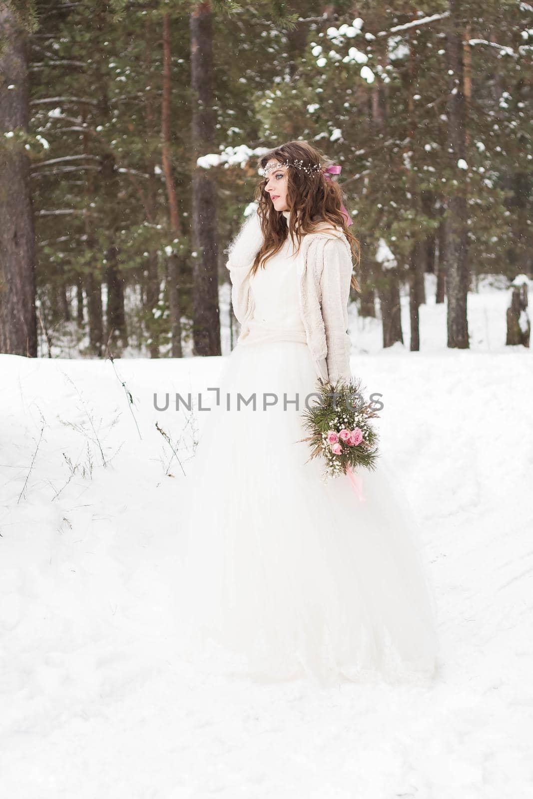 Beautiful bride in a white dress with a bouquet in a snow-covered winter forest. Portrait of the bride in nature.