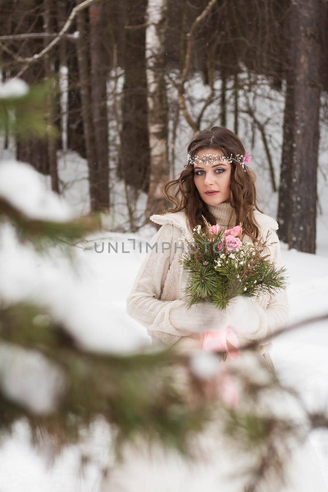 Beautiful bride in a white dress with a bouquet in a snow-covered winter forest. Portrait of the bride in nature.