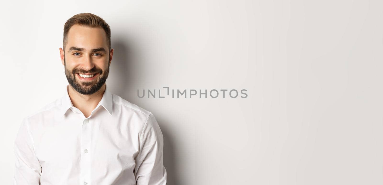 Close-up of confident male employee in white collar shirt smiling at camera, standing self-assured against studio background.