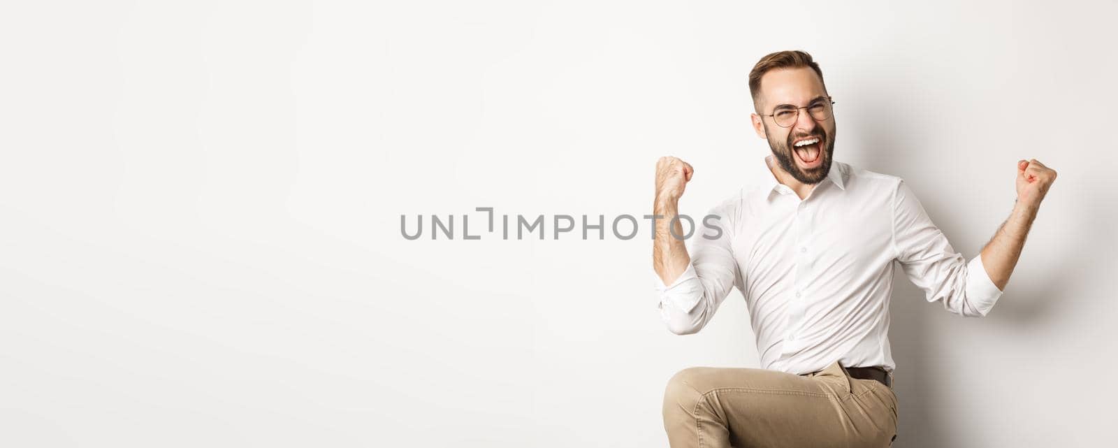 Successful businessman rejoicing, raising hands up and celebrating victory, winning something, standing over white background.