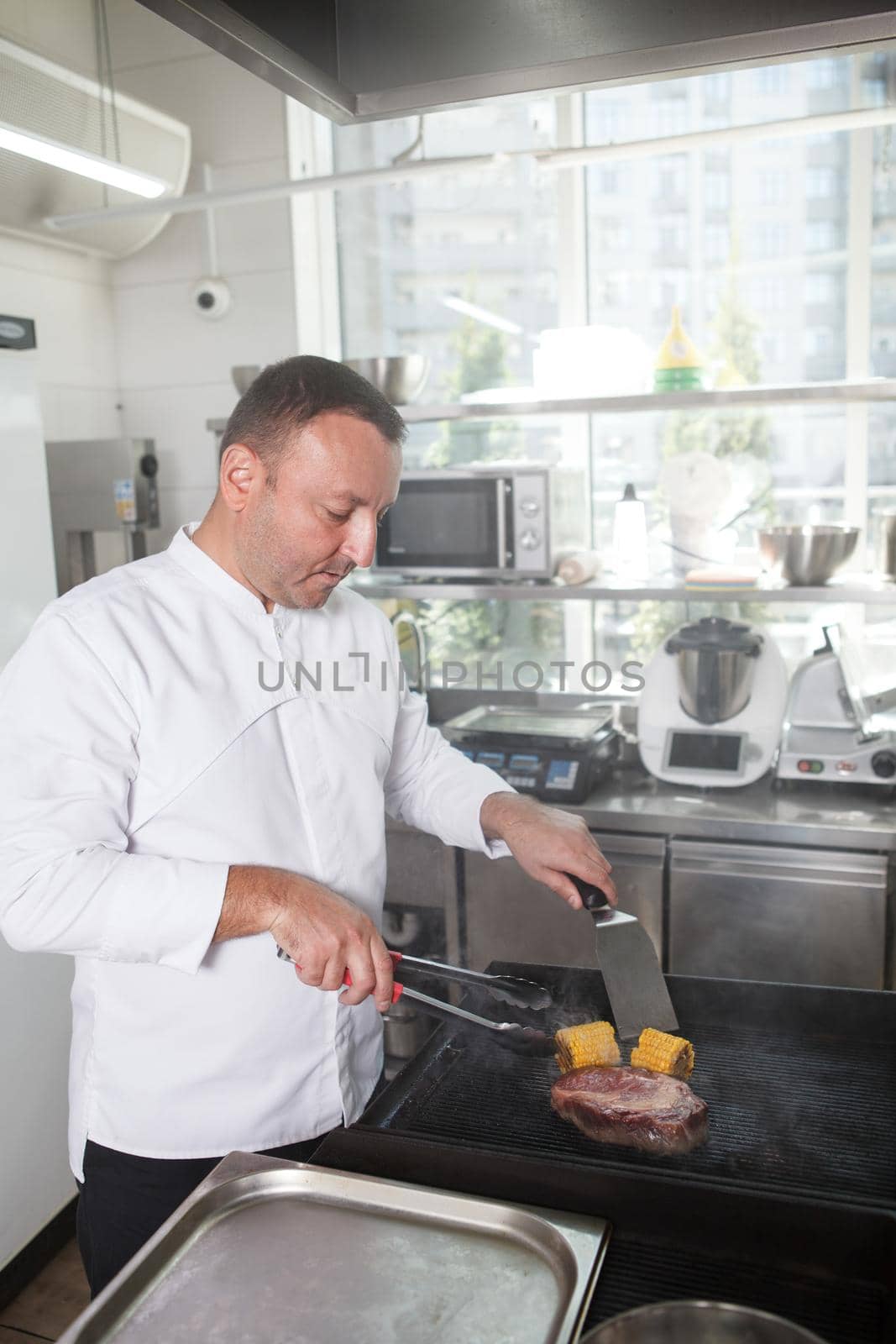 Vertical portrait of a professional chef preparing beef and corn on a grill at restaurant