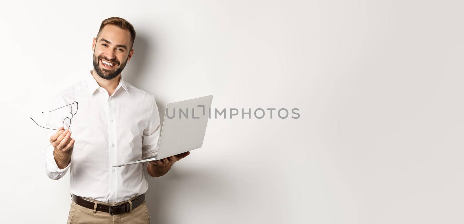 Satisfied businessman praising good job while checking laptop, standing over white background. Copy space