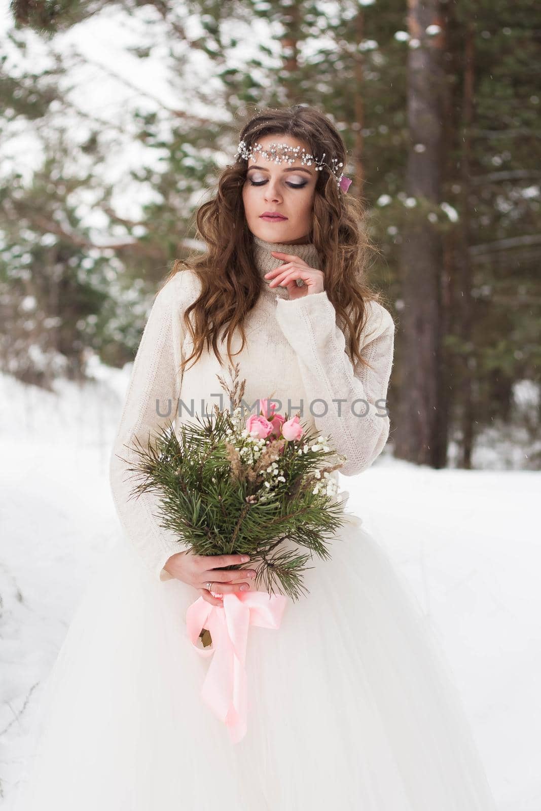 Beautiful bride in a white dress with a bouquet in a snow-covered winter forest. Portrait of the bride in nature.