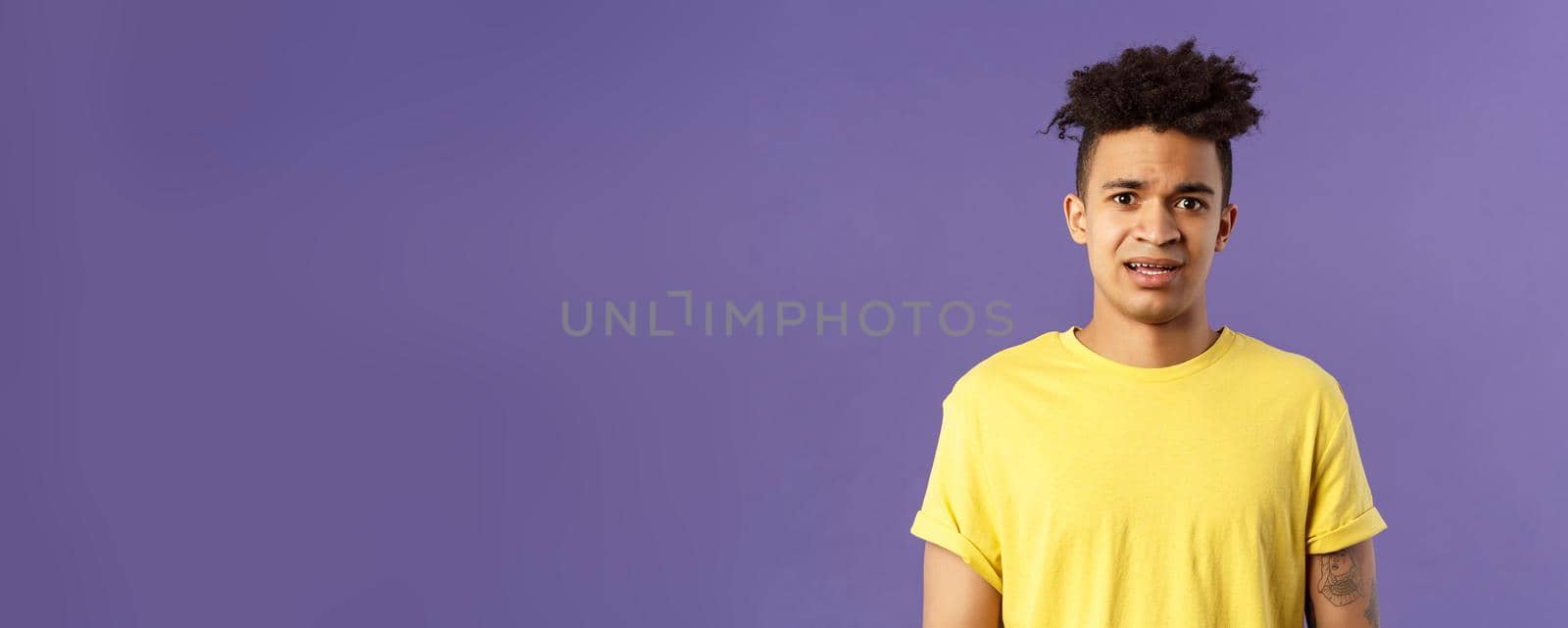Waist-up portrait of young concerned hispanic man with worried gaze looking at camera, frowning being scared for friend stuck in troublesome situation, want help, stand purple background.
