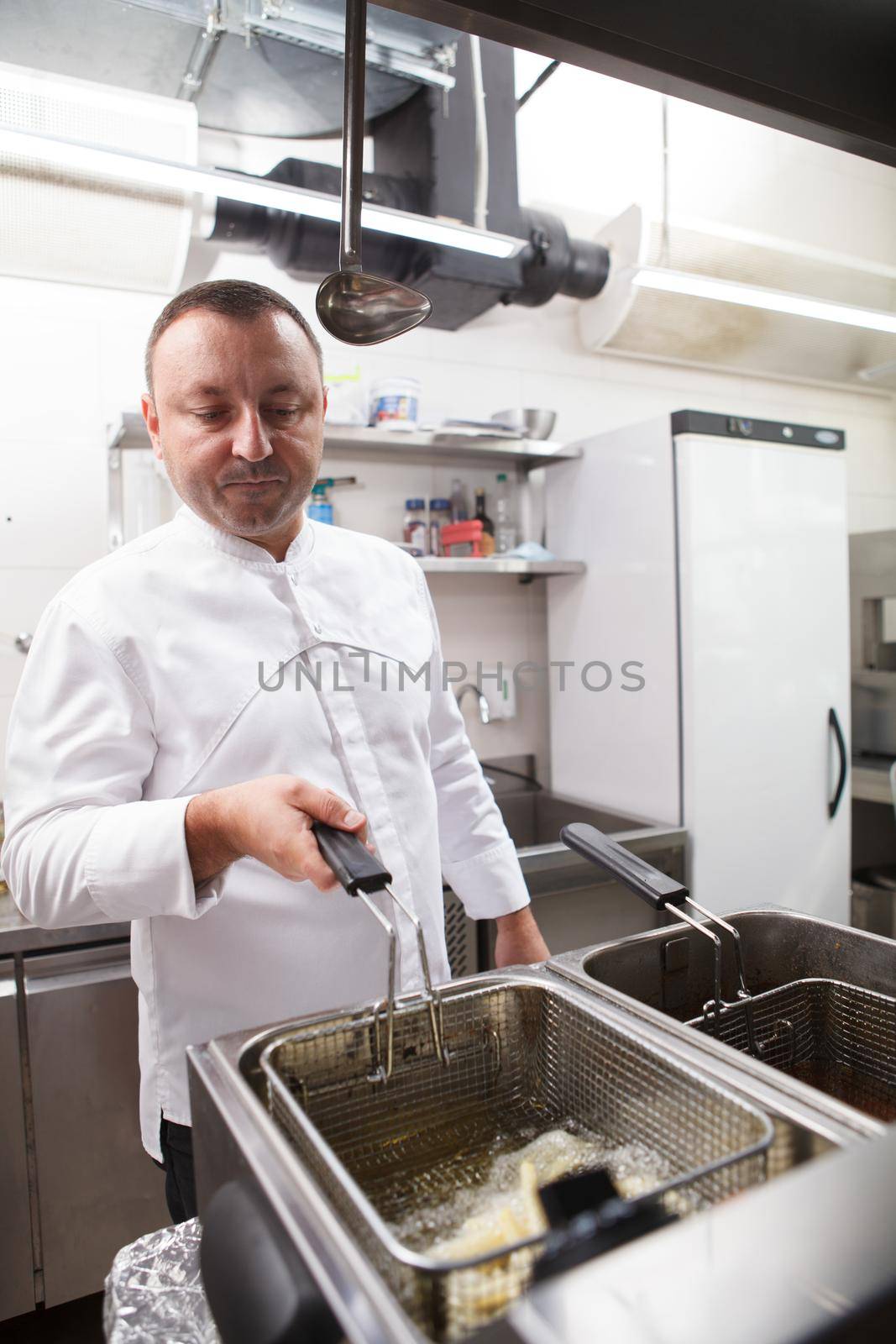 Vertical shot of a mature male chef frying french fries at the kitchen of his restaurant