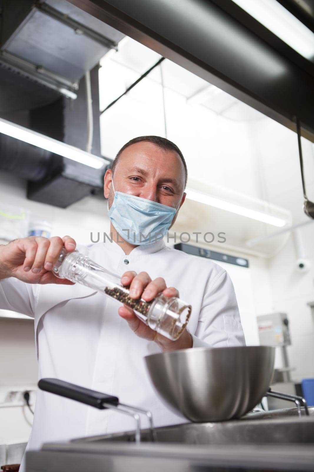 Vertical portrait of a chef in medical face mask salting prepared meal at restaurant kitchen