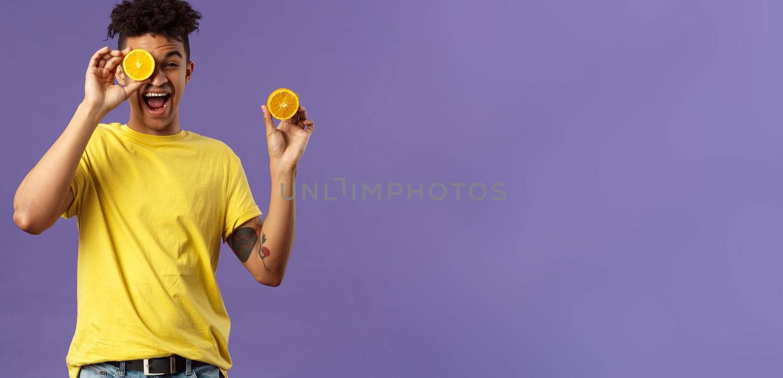 Holidays, vitamins and vacation concept. Portrait of carefree, upbeat good-looking man having fun, look playful laughing, likes eating fruits healthy food, holding pieces of oranges by Benzoix