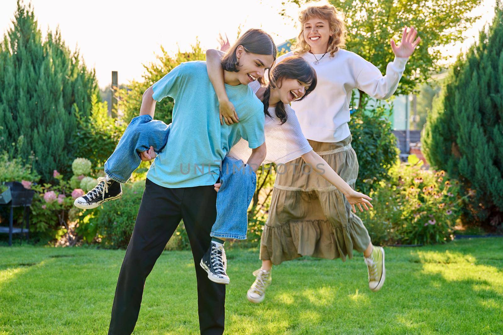 Three teenage friends having fun outdoor, sunny summer day on the lawn. Group of teenagers laughing together. Lifestyle, leisure, friendship, youth concept