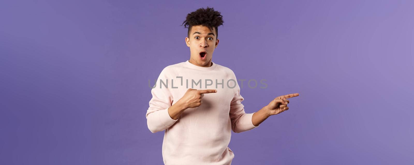 Portrait of excited, handsome young hispanic man talking about amazing party going nearby, describe incredible deal, open mouth wondered, pointing fingers right, recommend buy or download.