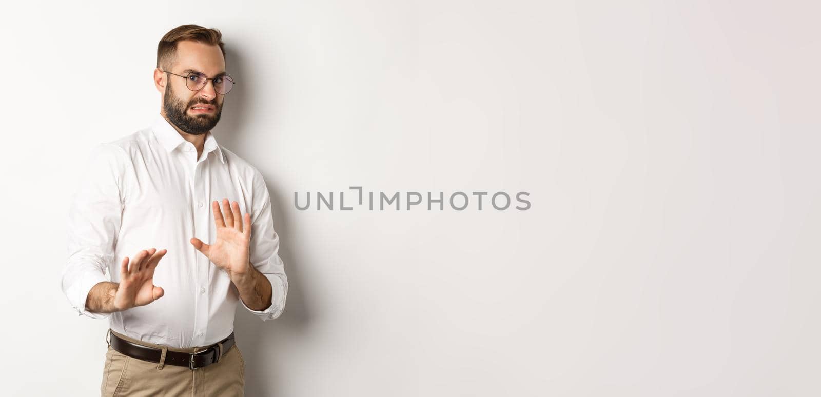 Disgusted businessman rejecting something bad, cringe from aversion, showing stop sign, standing over white background by Benzoix