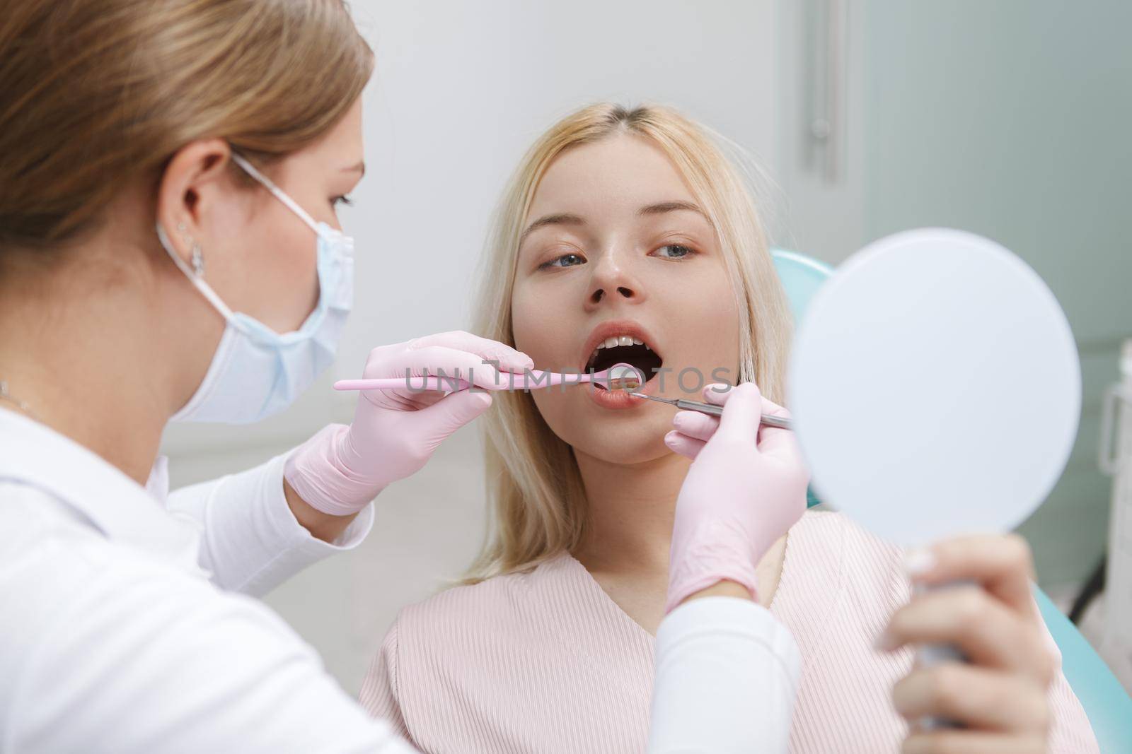 Woman looking into mirror while dentist checking her teeth