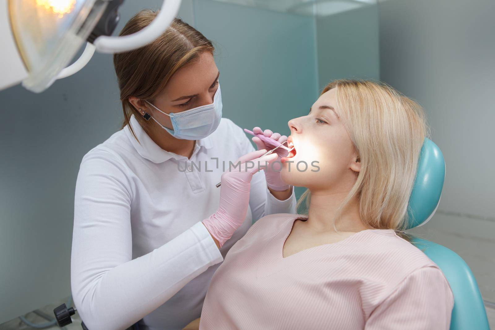 Professional dentist wearing medical face mask, examining teeth of female patient