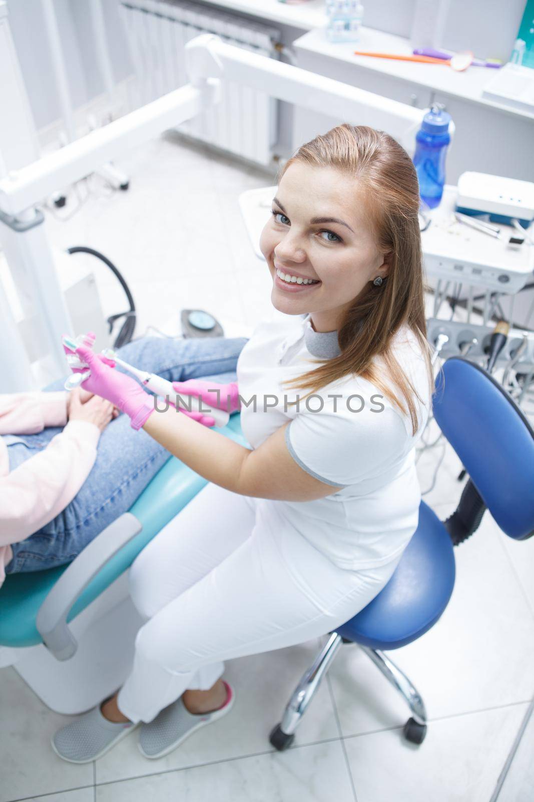 Vertical top view shot of a beautiful cheerful female dentist smiling to camera while working with patient