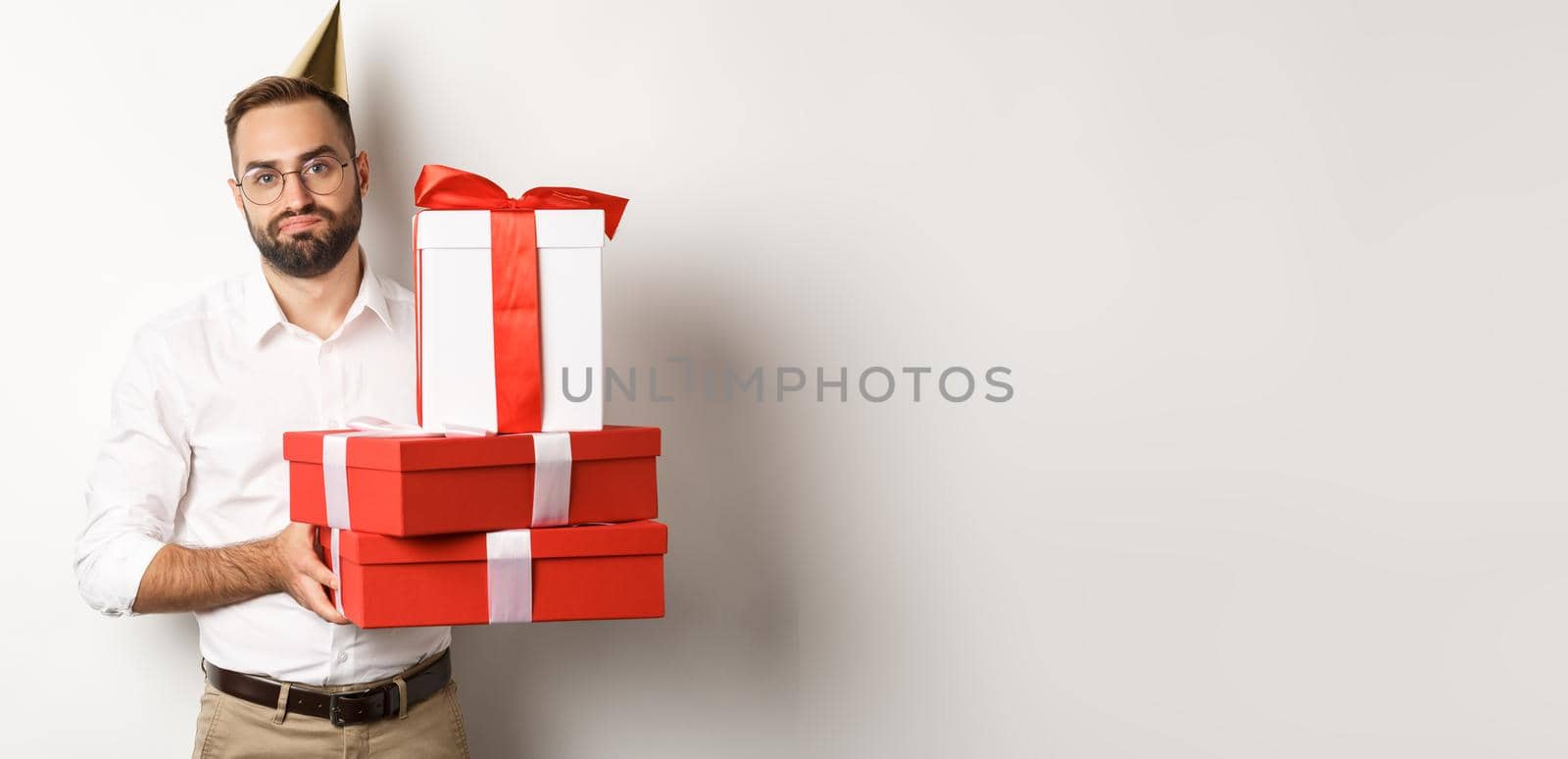 Holidays and celebration. Displeased guy holding birthday gifts and looking disappointed, dislike presents, standing over white background.