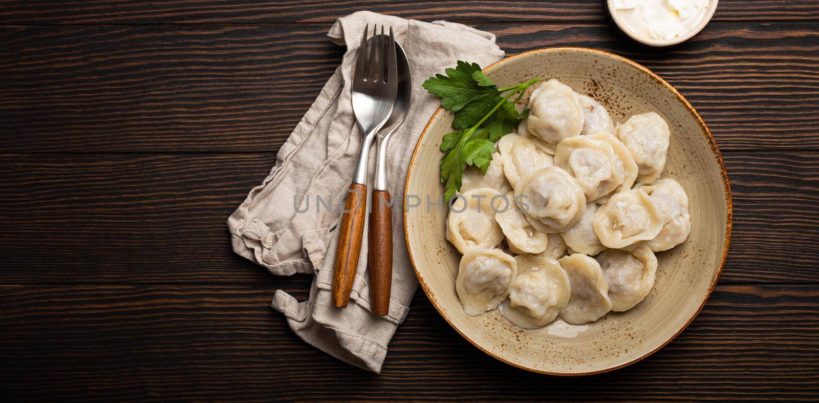 Pelmeni, traditional dish of Russian cuisine, boiled dumplings with minced meat filling on plate with sour cream sauce on wooden rustic background table from above food composition space for text