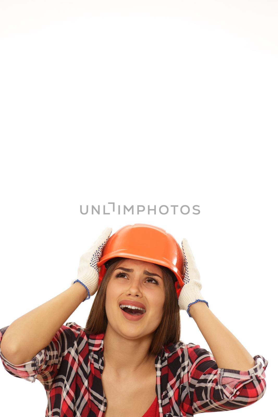 Vertical portrait of ayoung female engineer in protective helmet screaming looking at the copy space above. Terrified female contractor shouting isolated. Scared woman in a hardhat