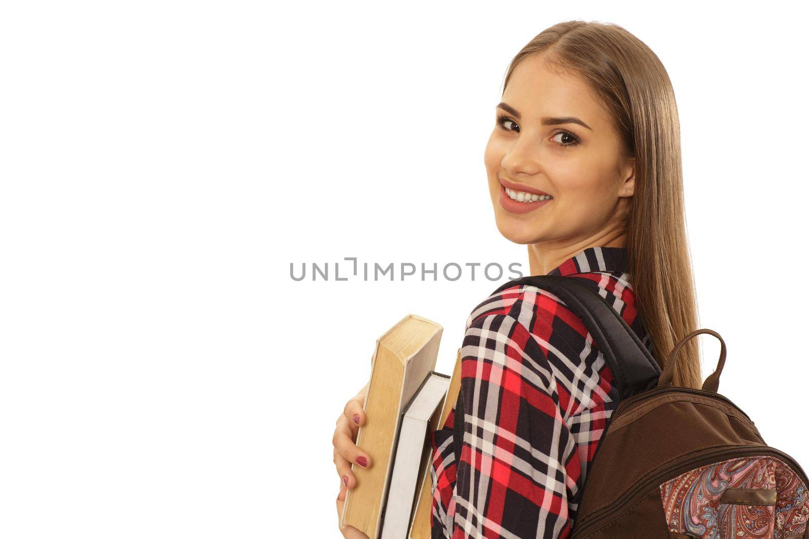Gorgeous cheerful young woman student smiling over her shoulder wearing a backpack holding her books. Happy female learner isolated on white copy space. Studying, learning, scholarship, graduation