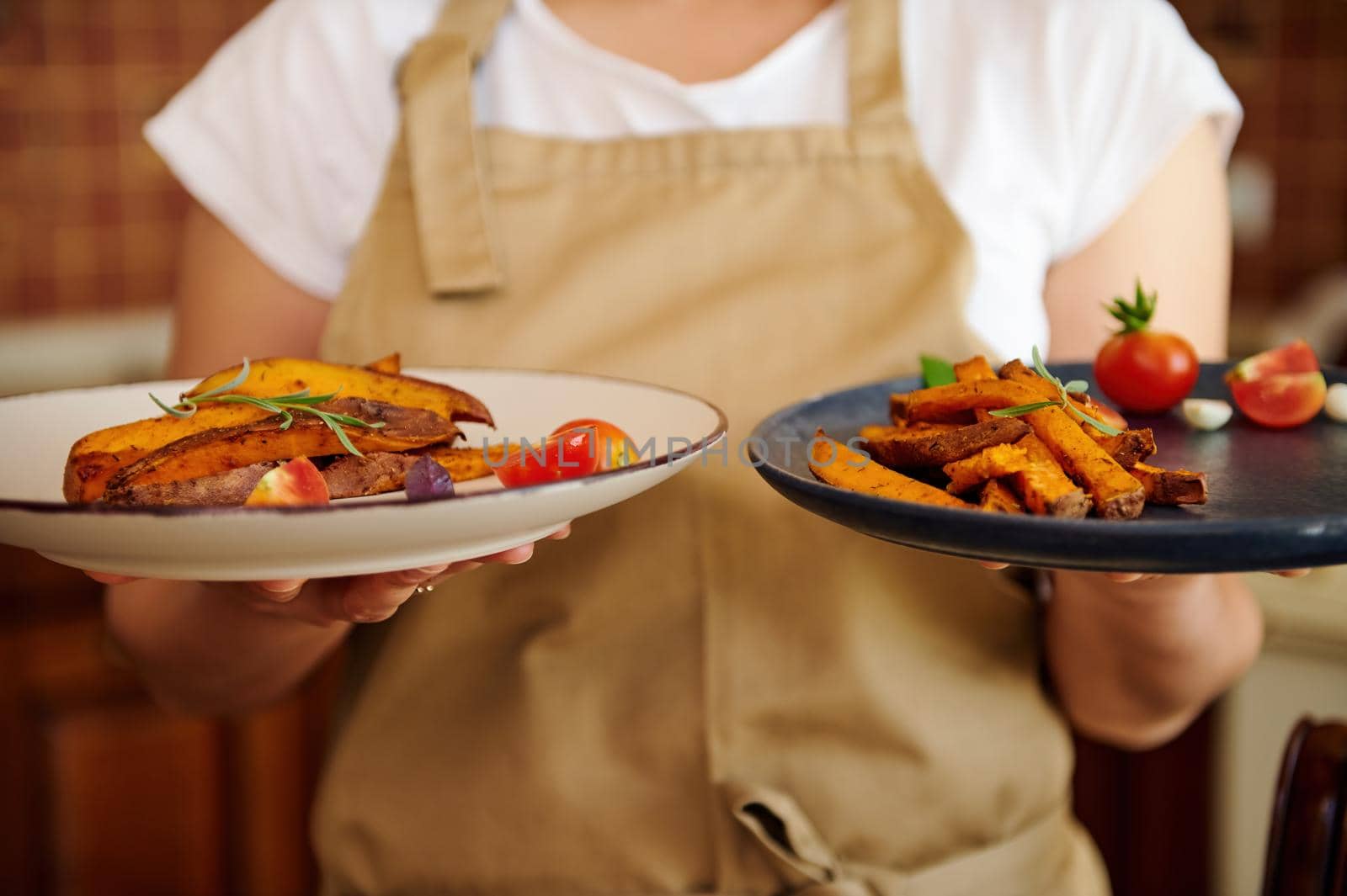 Focus on plates with fried slices of organic batata or sweet potato wedges drizzled with olive oil in chef's hands by artgf