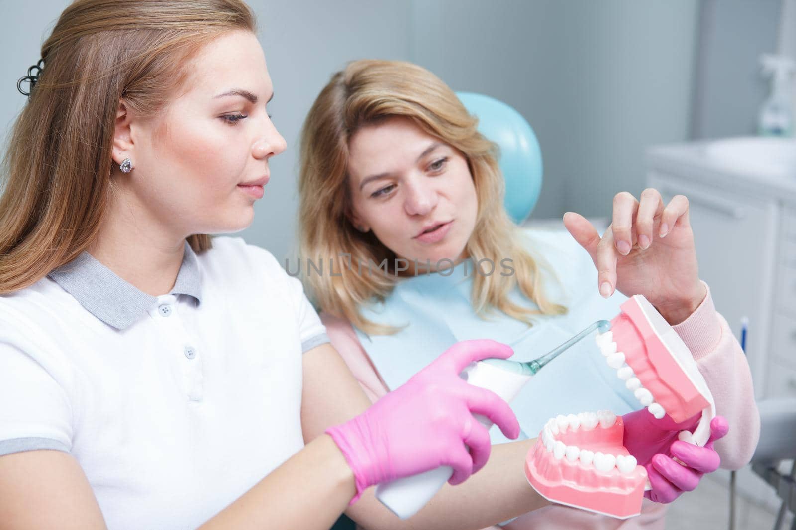 Young female dentist showing her patient ultrasonic toothbrush on jaw model