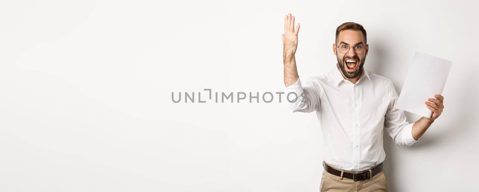 Angry businessman shouting and showing bad report, looking disappointed and frustrated, standing over white background.