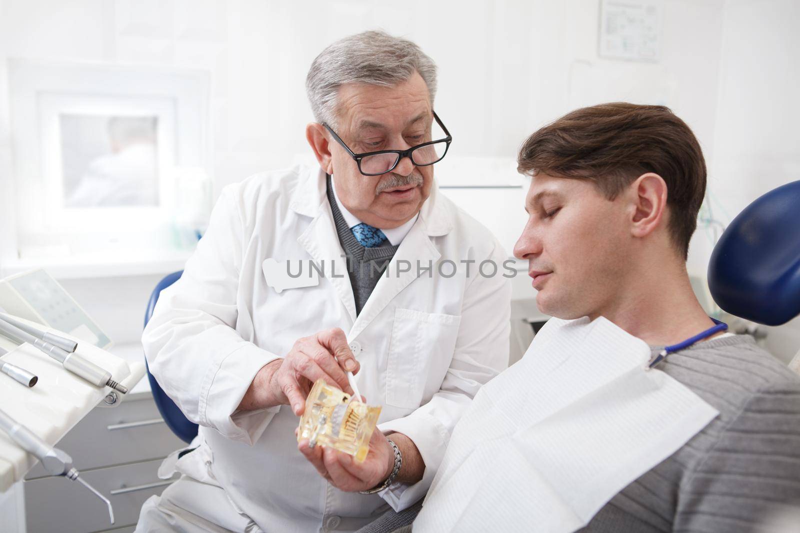 Elderly male dentist working at his clinic, talking to the patient