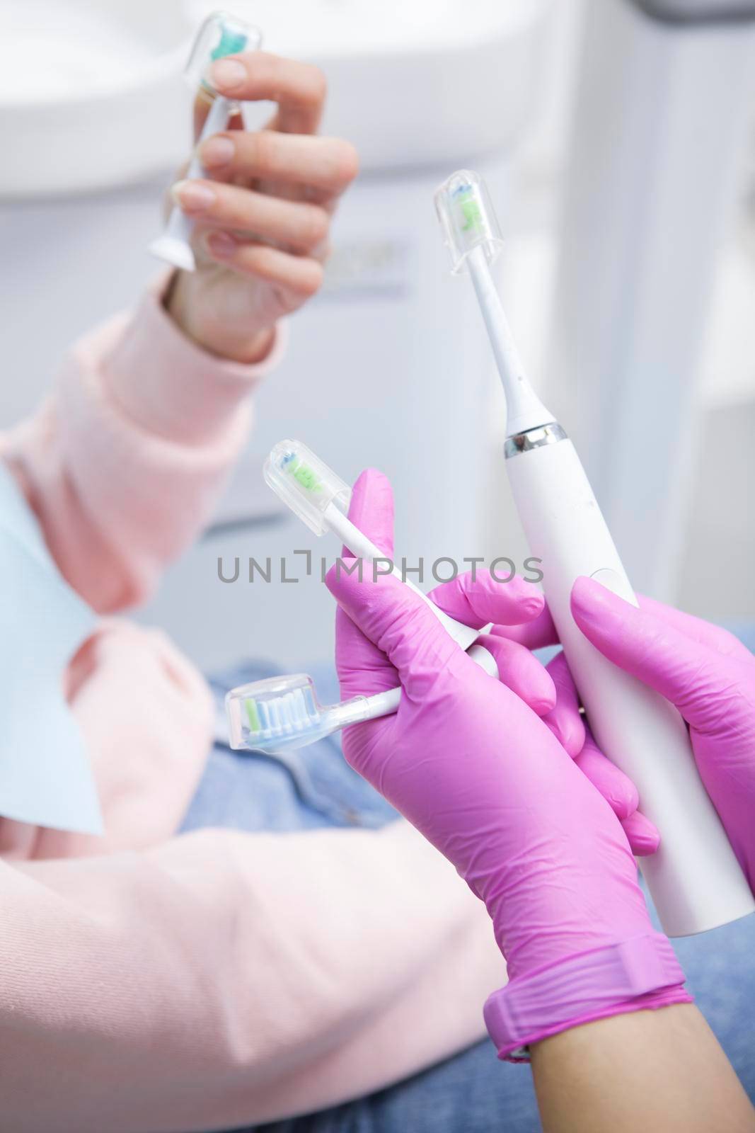 Vertical cropped shot of a dentist showing to her patient electric toothbrush with various replacement heads