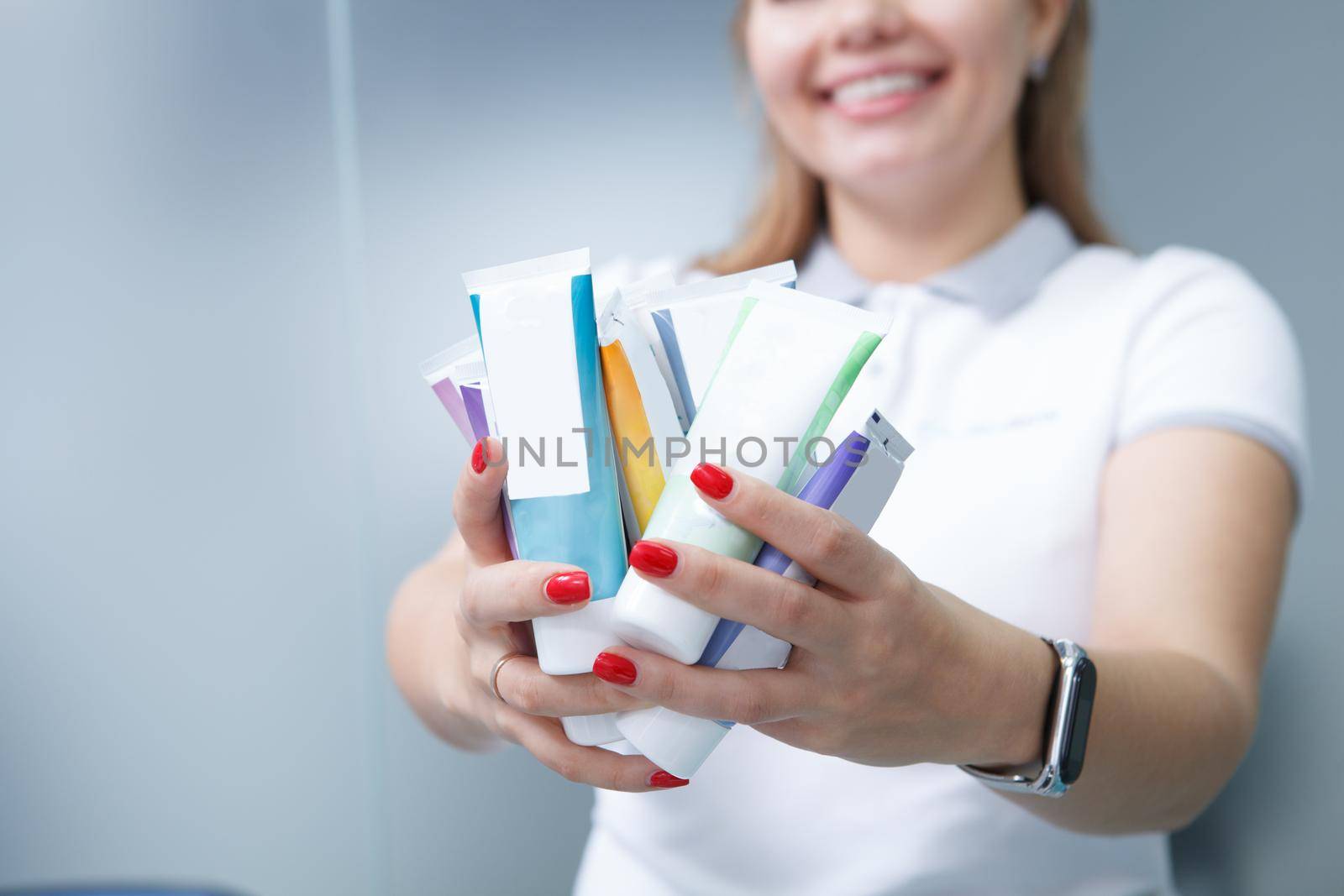 Cropped shot of female dentist smiling, holding out many toothpaste tubes to the camera