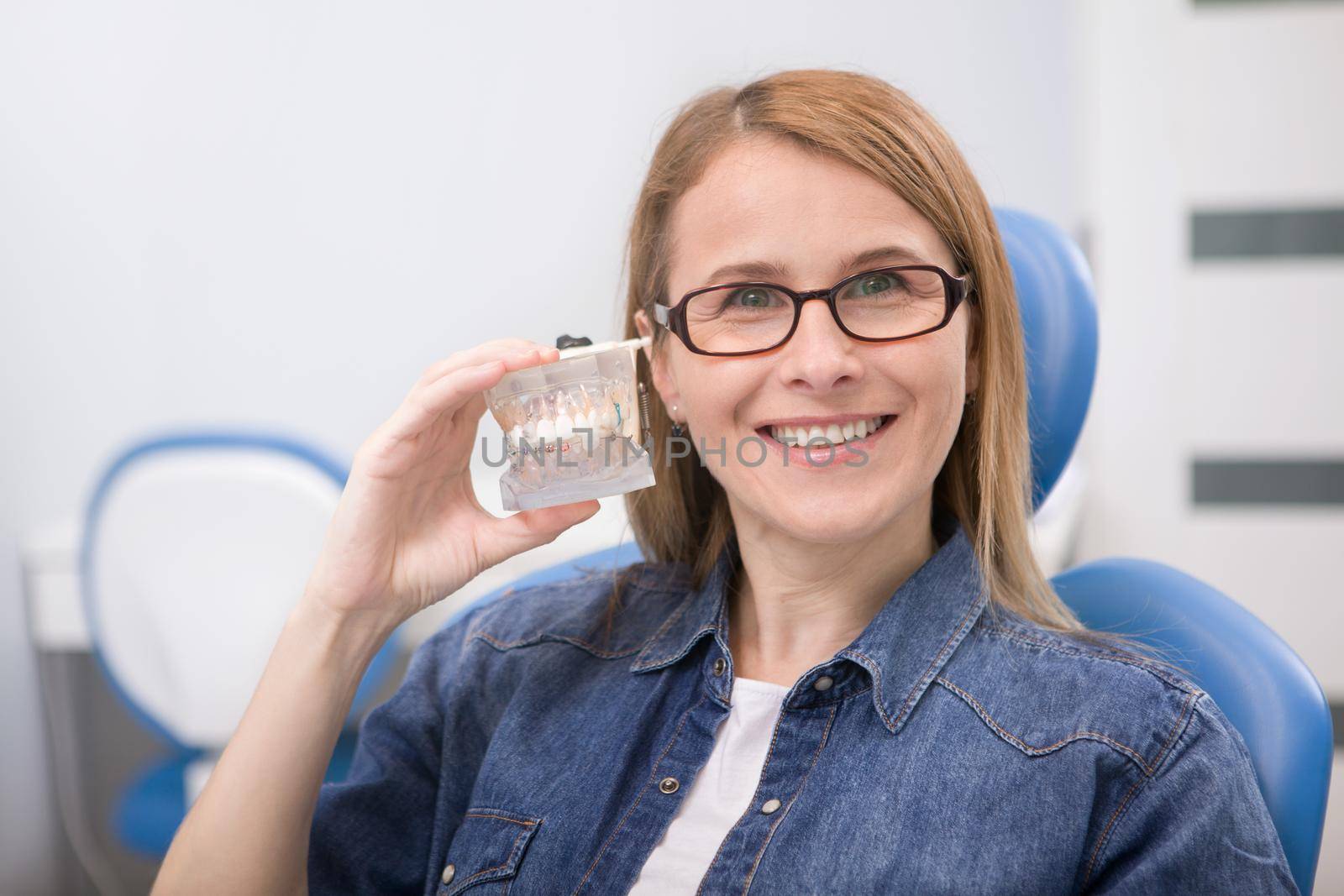 Happy mature woman with healthy white teeth smiling, holding jaw model with braces