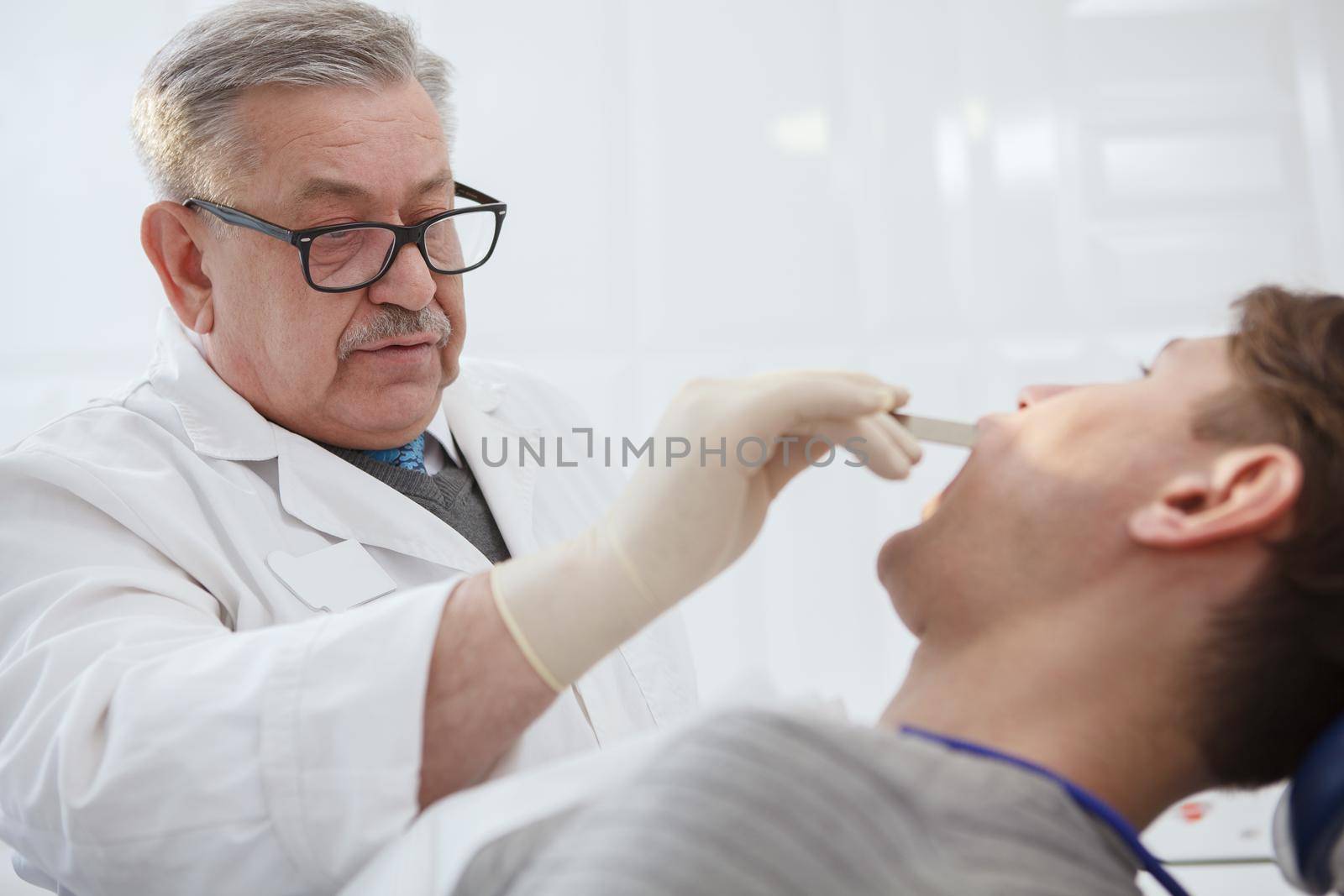 Close up of a senior male dentist examining teeth of a patient