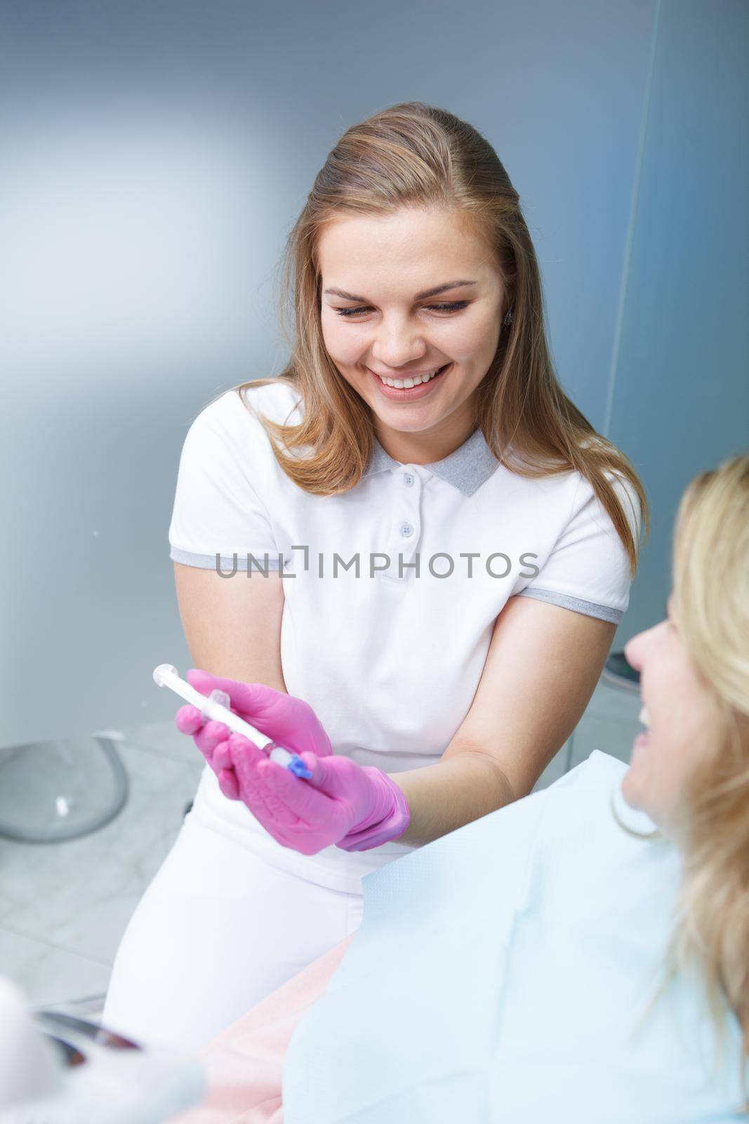 Vertical shot of a young female dentist showing teeth whitening gel to female patient