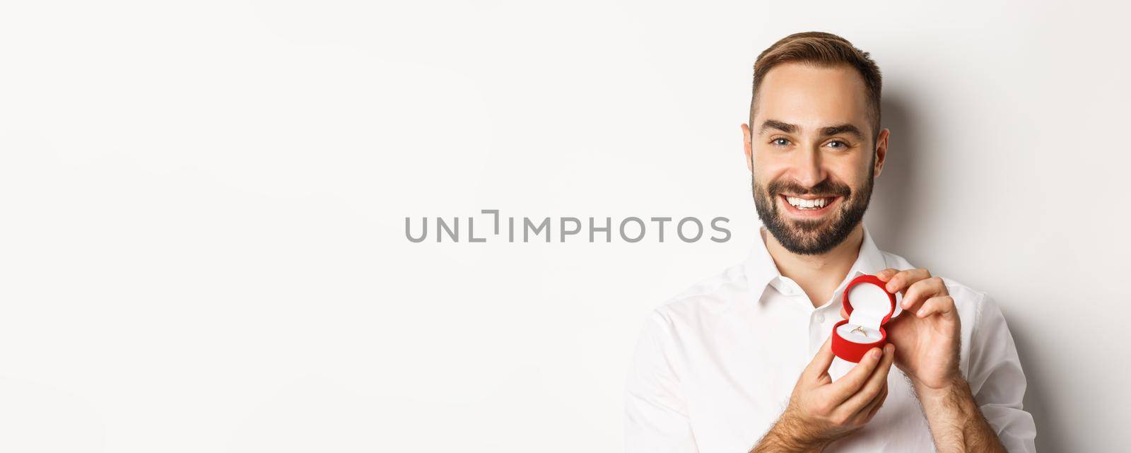 Close-up of happy handsome man making a proposal, holding wedding ring in box and smiling, asking to marry him, white background.