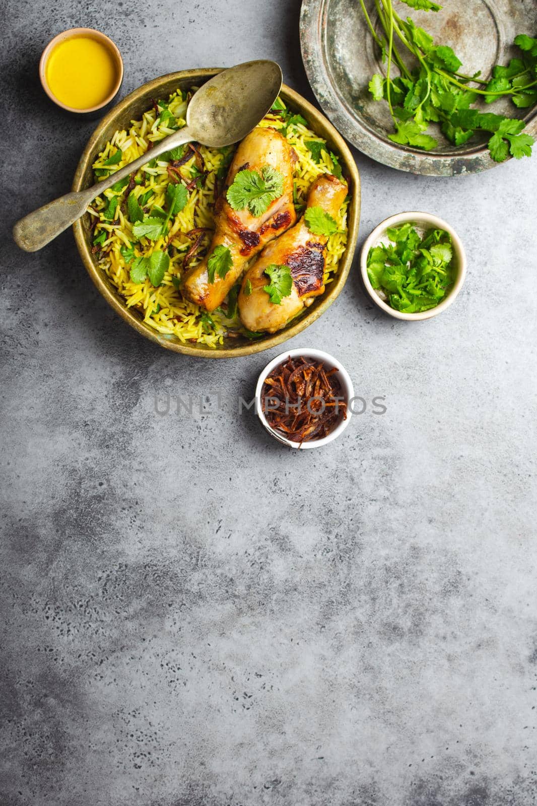 Biryani chicken, traditional dish of Indian cuisine, with basmati rice, fried onion, fresh cilantro in bowl on gray rustic stone background. Authentic Indian meal, top view, close-up, space for text