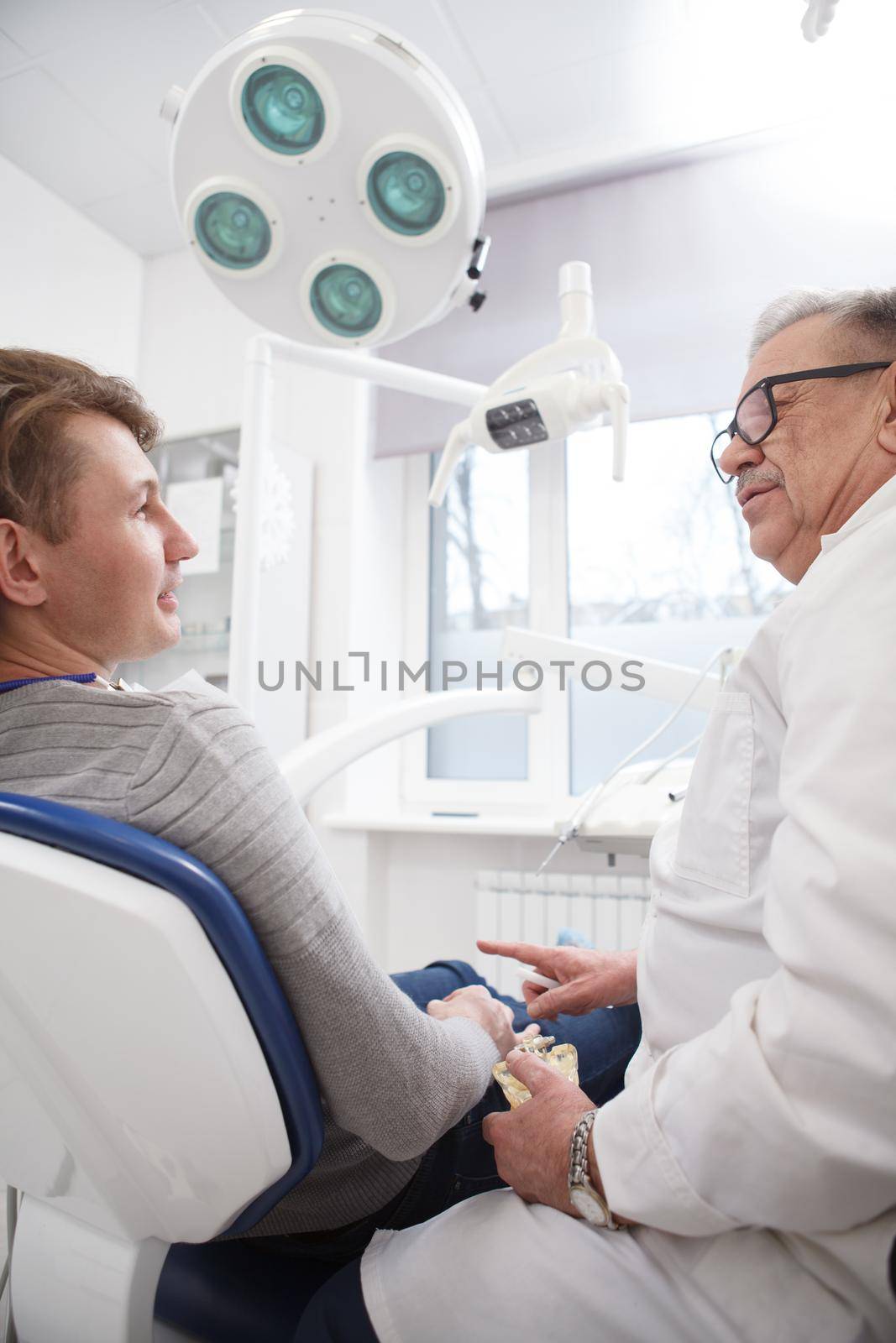 Low angle vertical shot of a man talking to his experienced dentist at dental office