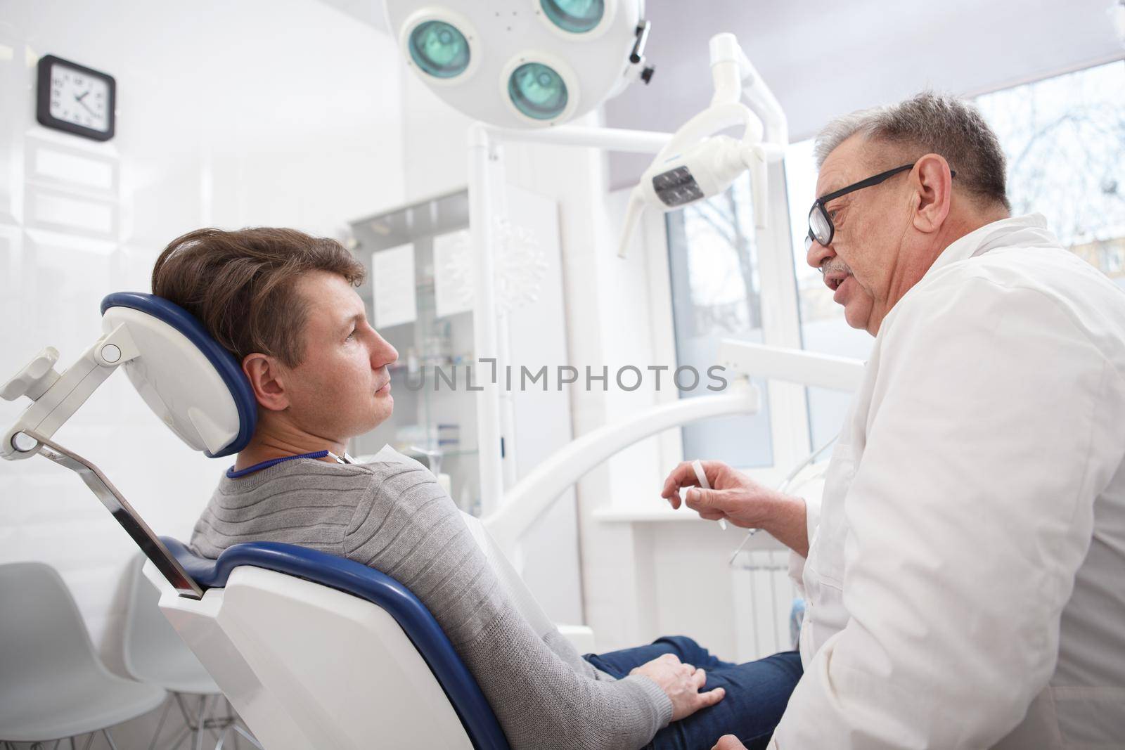 Elderly male dental surgeon talking to patient at dental office