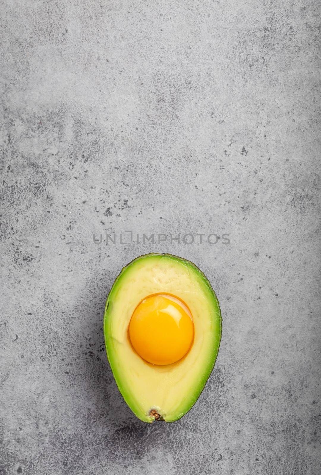 Foods rich in healthy fats for balanced nutrition: raw egg yolk in fresh cut half avocado on gray stone background. Ketogenic low carbs diet or clean eating concept, top view with space for text .