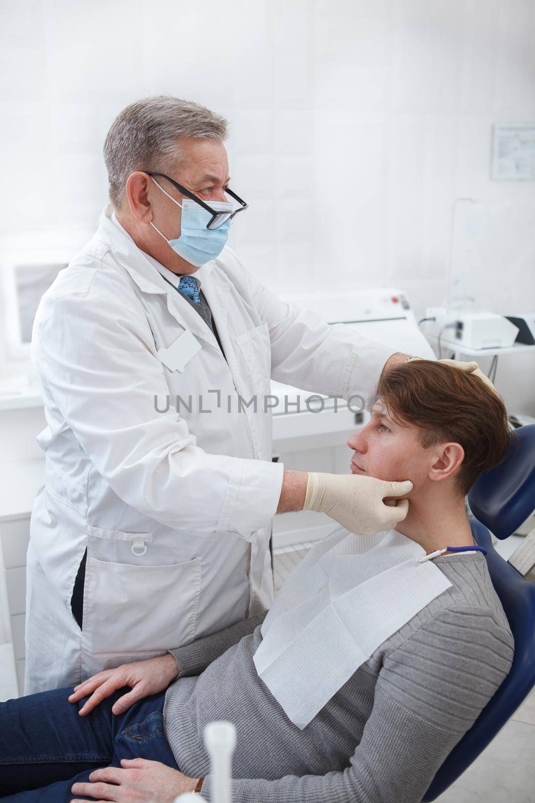 Vertical shot of a professional dentist wearing medical face mask, examining lymphatic nods of patient prior to dental treatment