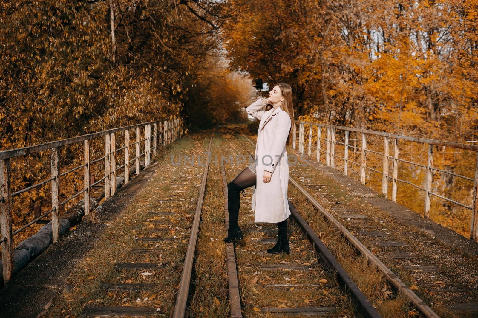 A beautiful long-haired woman walks through the autumn streets. Railway, autumn leaves, a woman in a light coat.