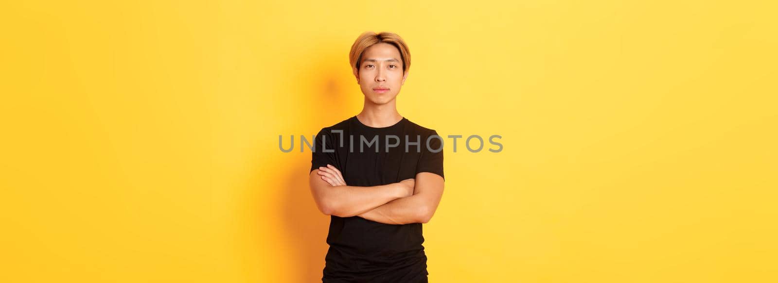 Portrait of serious-looking confident asian guy in black t-shirt, cross arms chest, standing yellow background by Benzoix