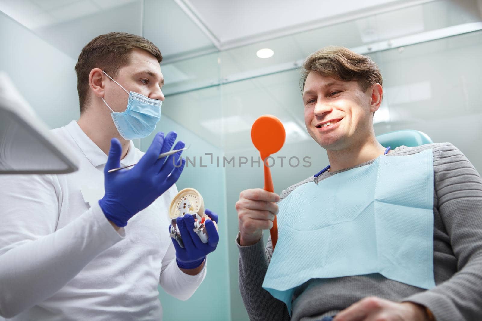 Low angle shot of a cheerful man checking his teeth in the mirror after dental examination at dental clinic